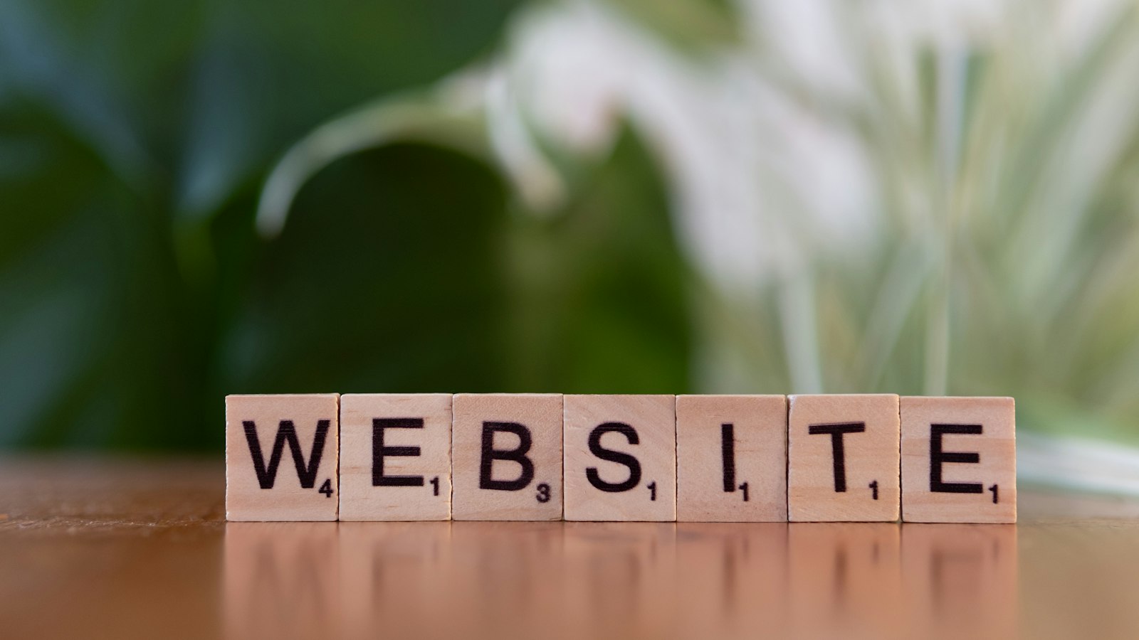 Wooden letter tiles spelling WEBSITE on a table in front of green plants.